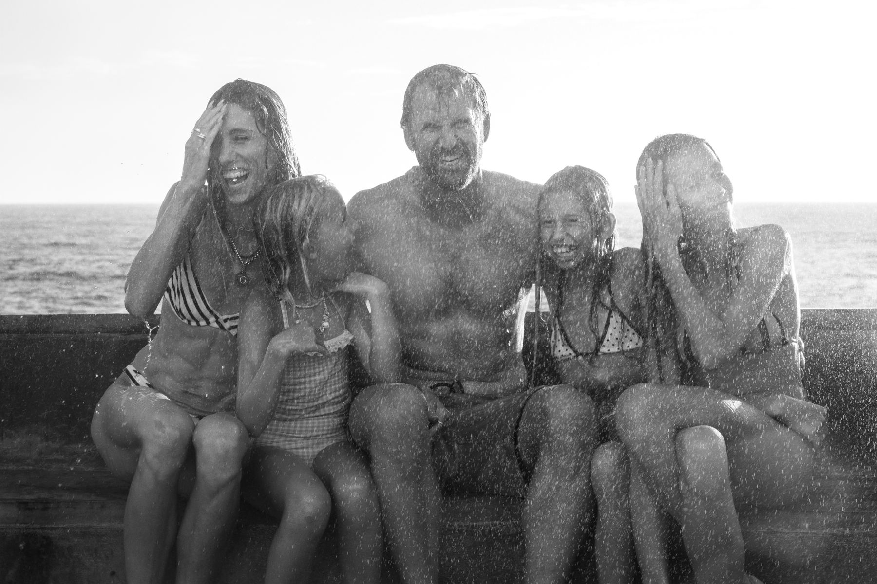 A family laughing together on a seawall as ocean spray falls around them